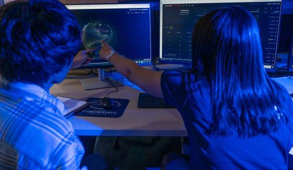 Two students in a computer lab look at an image of a global map.